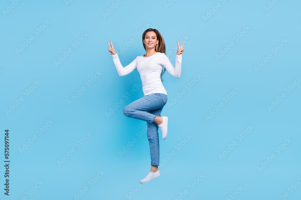 Full length photo of pretty sweet woman wear white shirt jumping high showing v-signs isolated blue color background