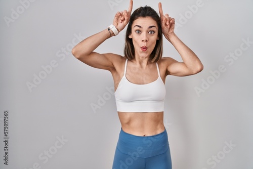 Hispanic woman wearing sportswear over isolated background doing funny gesture with finger over head as bull horns © Krakenimages.com
