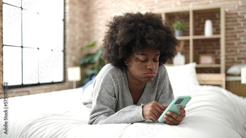 African american woman using smartphone lying on bed at bedroom