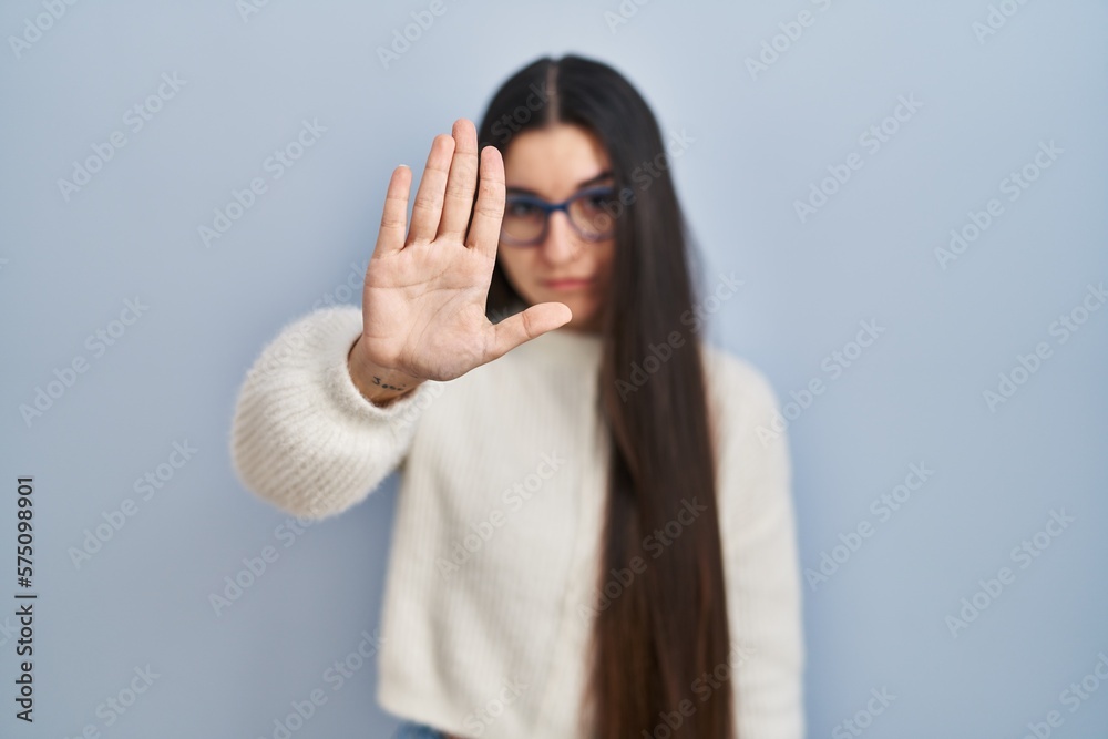 Young hispanic woman wearing casual sweater over blue background doing stop sing with palm of the hand. warning expression with negative and serious gesture on the face. Young hispanic woman wearing casual sweater over blue background doing stop sing with palm of the hand. warning expression with negative and serious gesture on the face.