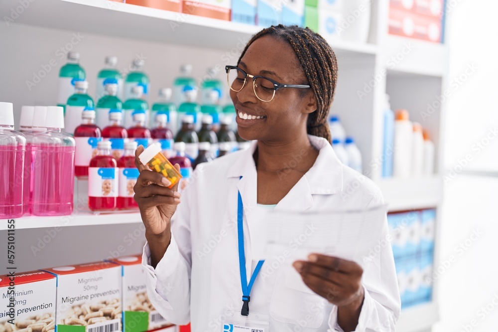 African american woman pharmacist holding pills bottle reading prescription at pharmacy