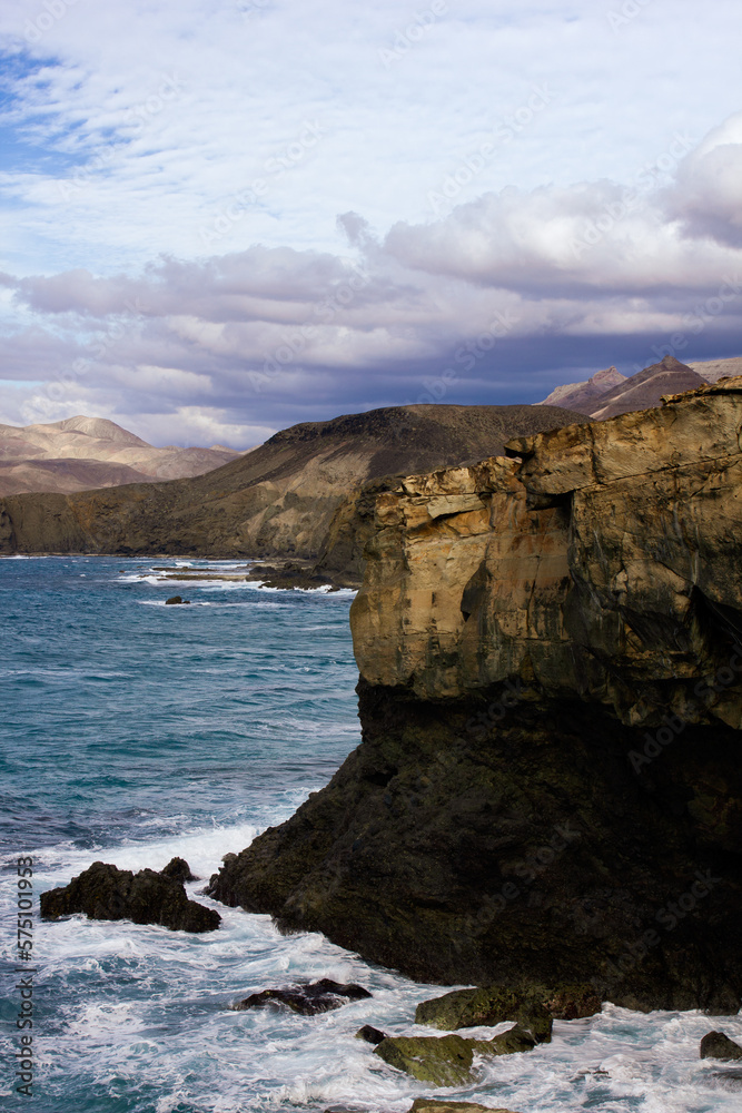 The rocky cliffside of Fuerteventura  with waves crashing into the rocks and clouds up above