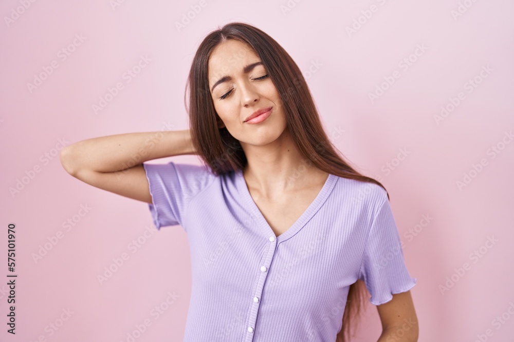 Young hispanic woman with long hair standing over pink background suffering of neck ache injury, touching neck with hand, muscular pain Young hispanic woman with long hair standing over pink background suffering of neck ache injury, touching neck with hand, muscular pain