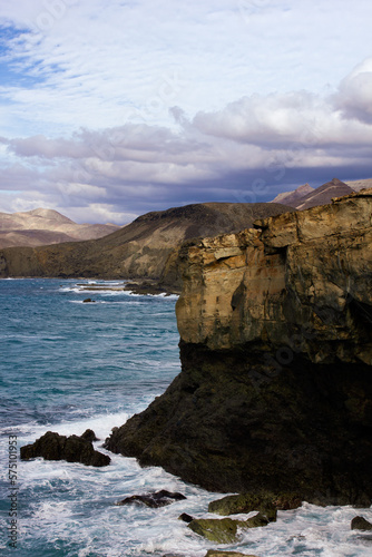 The rocky cliffside of Fuerteventura with waves crashing into the rocks and clouds up above