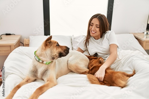 Young hispanic woman playing with dogs lying on bed at bedroom