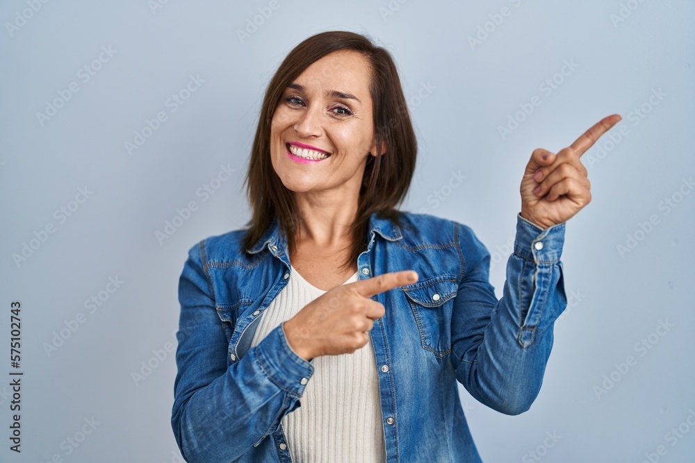 Middle age brunette woman wearing casual denim jacket over isolated background smiling and looking at the camera pointing with two hands and fingers to the side. Middle age brunette woman wearing casual denim jacket over isolated background smiling and looking at the camera pointing with two hands and fingers to the side.