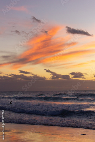 A beautiful sunset view of the beach with surfers in the water and orange clouds above in Fuerteventura