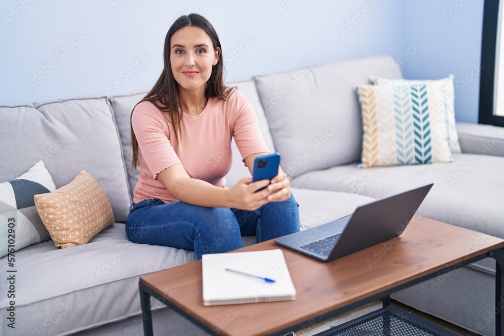 Young beautiful hispanic woman using smartphone and laptop at home Young beautiful hispanic woman using smartphone and laptop at home