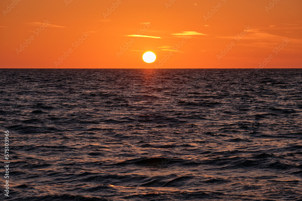 Ocean sunset. Big white sun on dramatic bright sky background, soft evening cloud over sea dark water