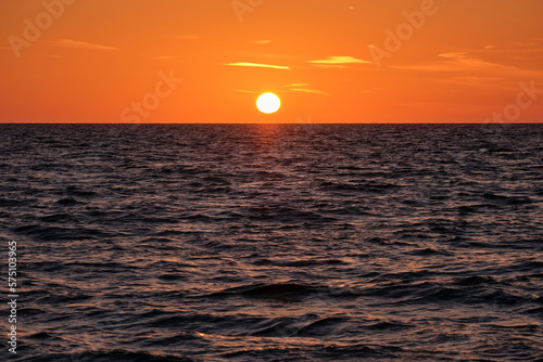 Ocean sunset. Big white sun on dramatic bright sky background  soft evening cloud over sea dark water