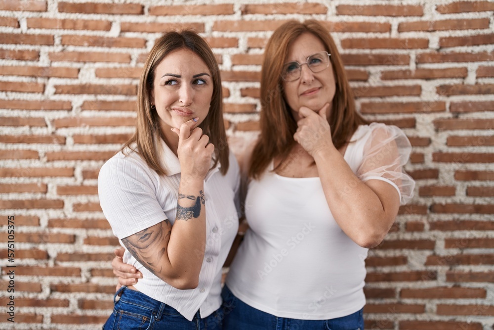 Hispanic mother and daughter wearing casual white t shirt looking confident at the camera smiling with crossed arms and hand raised on chin. thinking positive.