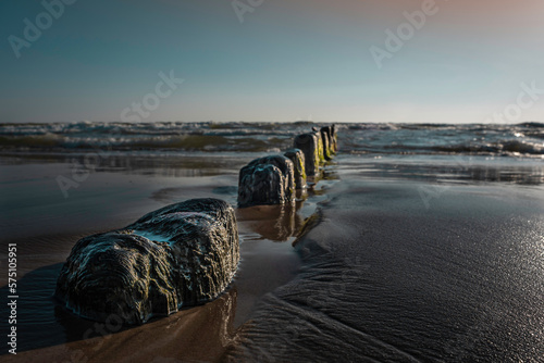 Ruins of an old bridge to the sea washed out by water and sand with a very calm sea in background