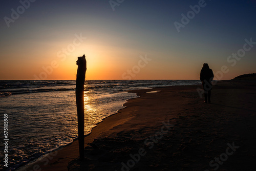 A woman walking away to the distance by the beach during beautiful red sunset