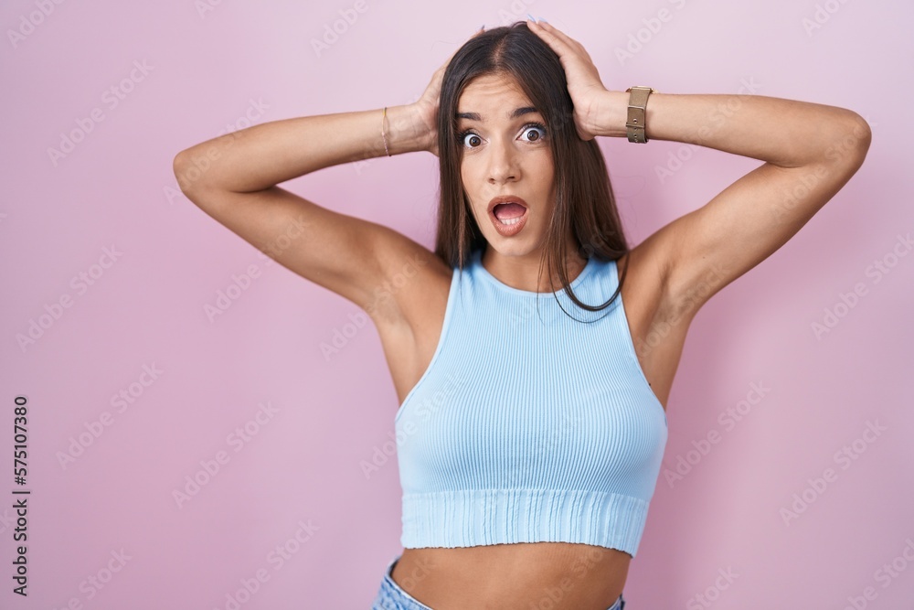 Young brunette woman standing over pink background crazy and scared with hands on head, afraid and surprised of shock with open mouth Young brunette woman standing over pink background crazy and scared with hands on head, afraid and surprised of shock with open mouth