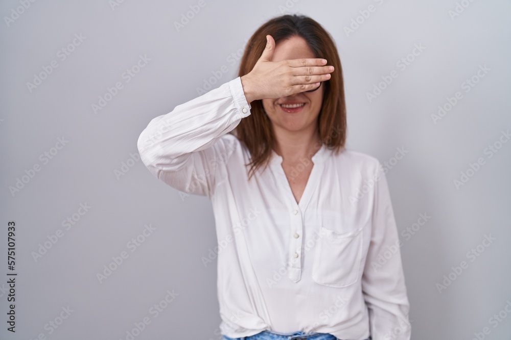 Brunette woman standing over white isolated background smiling and laughing with hand on face covering eyes for surprise. blind concept. Brunette woman standing over white isolated background smiling and laughing with hand on face covering eyes for surprise. blind concept.