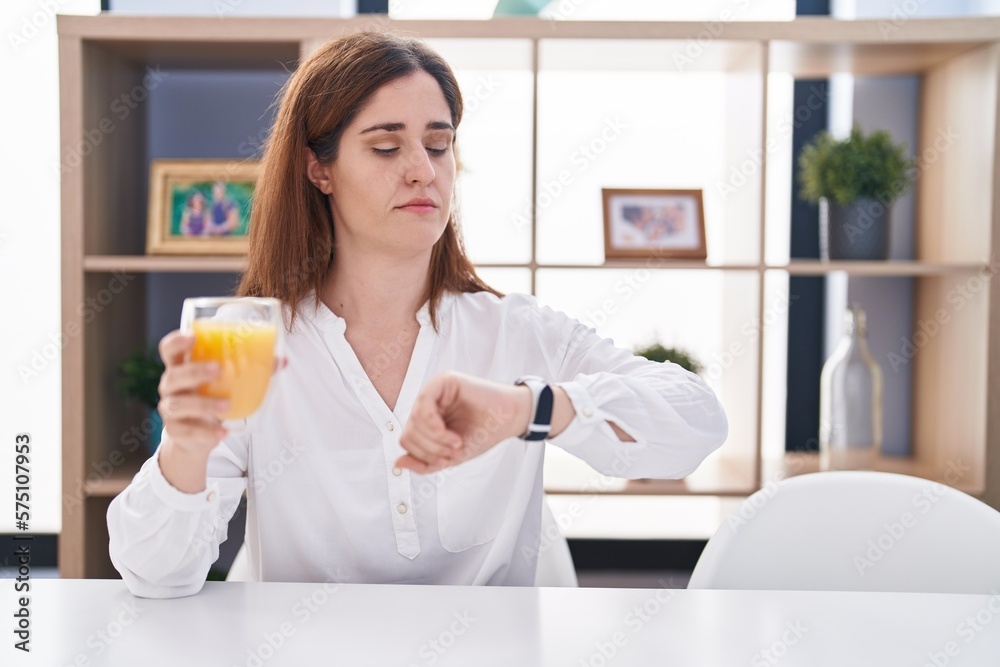 Brunette woman drinking glass of orange juice checking the time on wrist watch, relaxed and confident Brunette woman drinking glass of orange juice checking the time on wrist watch, relaxed and confident