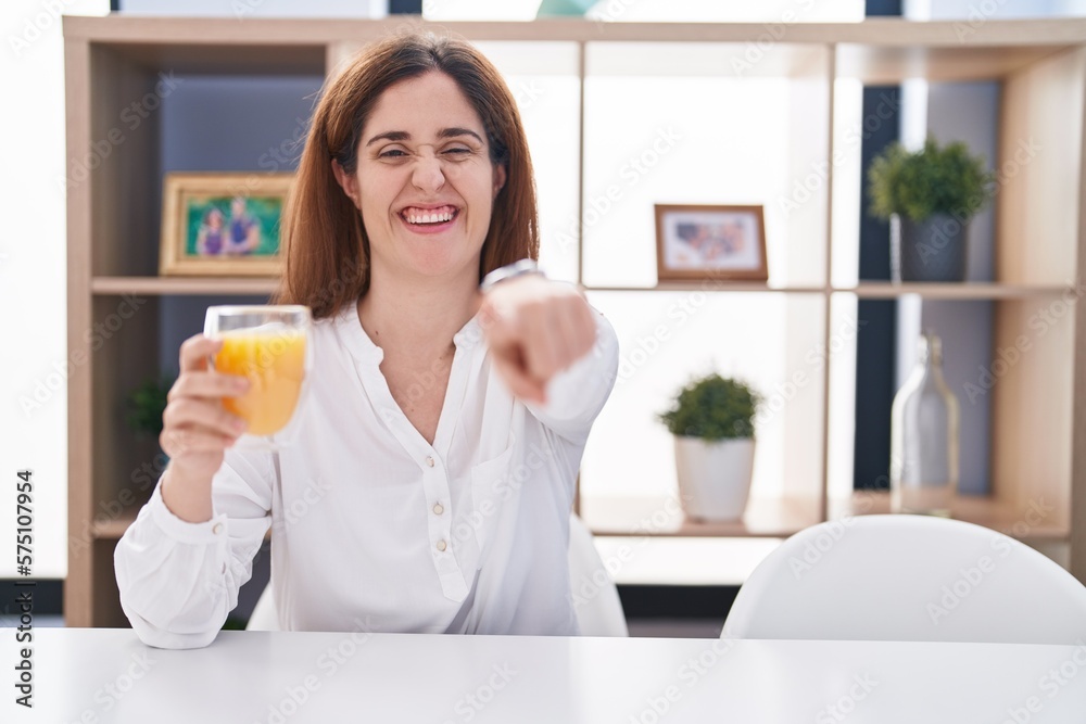 Brunette woman drinking glass of orange juice pointing to you and the camera with fingers, smiling positive and cheerful Brunette woman drinking glass of orange juice pointing to you and the camera with fingers, smiling positive and cheerful