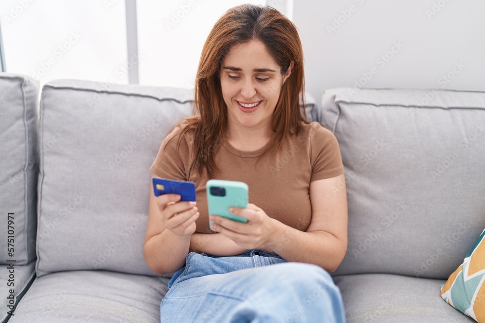 Young woman using smartphone and credit card sitting on sofa at home Young woman using smartphone and credit card sitting on sofa at home