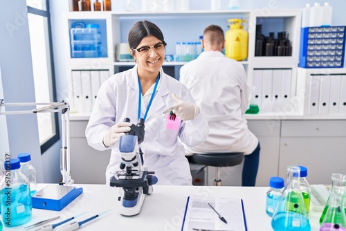 Young woman working at scientist laboratory smiling happy pointing with hand and finger