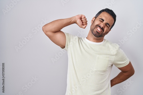 Hispanic man with beard standing over isolated background stretching back, tired and relaxed, sleepy and yawning for early morning