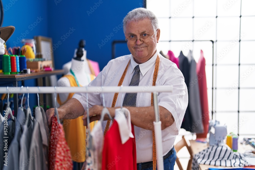 Middle age grey-haired man tailor smiling confident holding clothes on rack at tailor shop