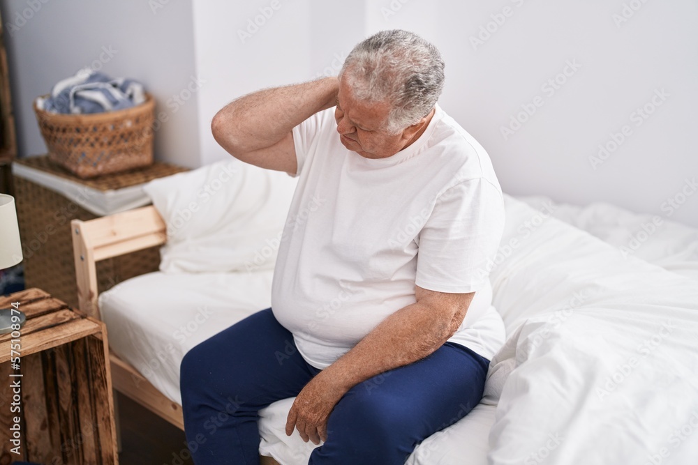 Middle age grey-haired man suffering for neck injury sitting on bed at bedroom Middle age grey-haired man suffering for neck injury sitting on bed at bedroom