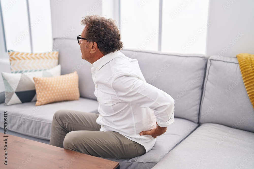 Middle age man suffering for backache sitting on sofa at home Middle age man suffering for backache sitting on sofa at home