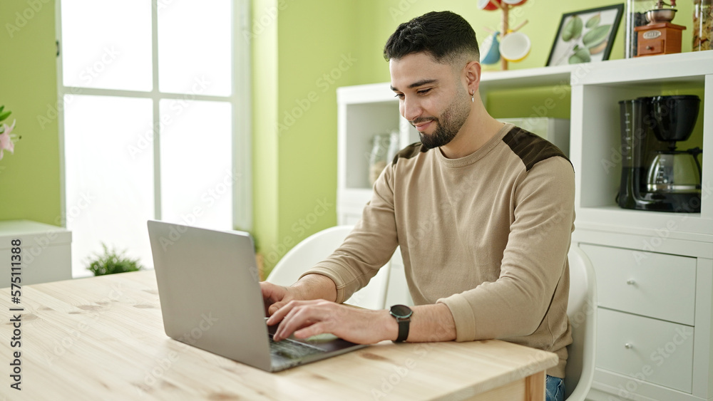 Young arab man using laptop sitting on table at home Young arab man using laptop sitting on table at home