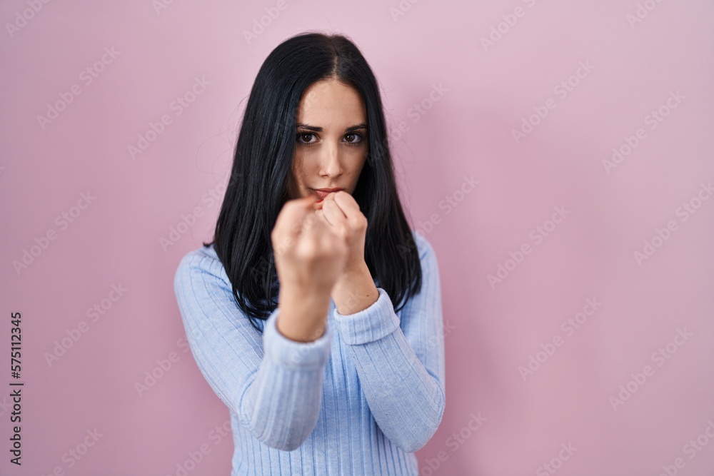 Hispanic woman standing over pink background ready to fight with fist defense gesture, angry and upset face, afraid of problem Hispanic woman standing over pink background ready to fight with fist defense gesture, angry and upset face, afraid of problem