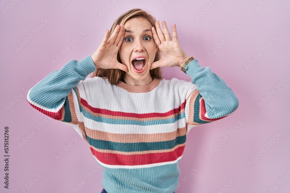 Young blonde woman standing over pink background smiling cheerful playing peek a boo with hands showing face. surprised and exited Young blonde woman standing over pink background smiling cheerful playing peek a boo with hands showing face. surprised and exited