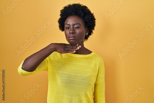African young woman standing over yellow studio cutting throat with hand as knife, threaten aggression with furious violence © Krakenimages.com