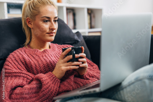 Caucasian woman holding a cup and looking at the laptop