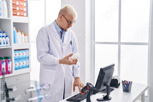 Wallpaper Mural Young caucasian man pharmacist holding pills bottle using computer at pharmacy Torontodigital.ca