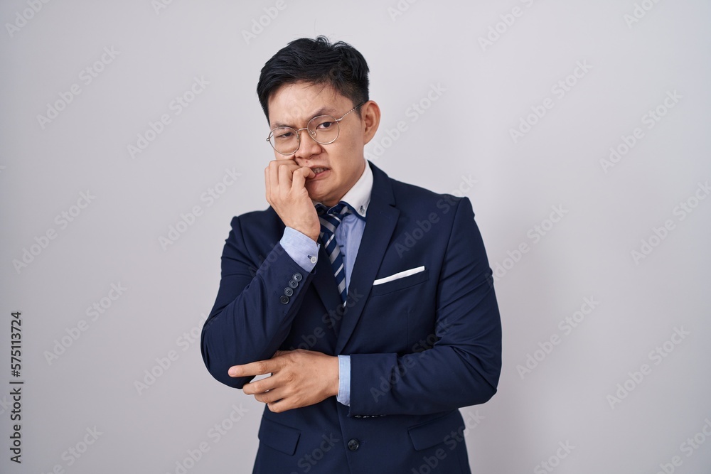 Young asian man wearing business suit and tie looking stressed and nervous with hands on mouth biting nails. anxiety problem. Young asian man wearing business suit and tie looking stressed and nervous with hands on mouth biting nails. anxiety problem.