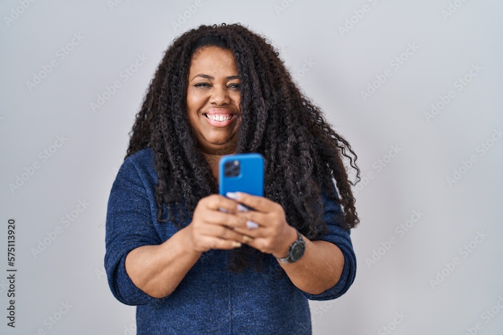 Plus size hispanic woman using smartphone typing message smiling with a happy and cool smile on face. showing teeth. Plus size hispanic woman using smartphone typing message smiling with a happy and cool smile on face. showing teeth.