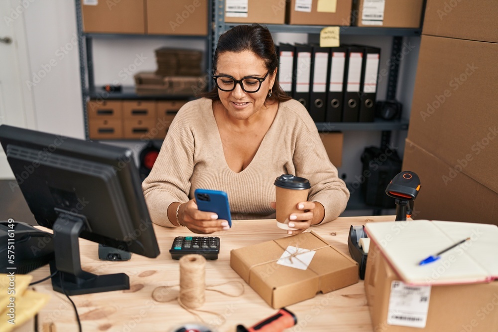 Middle age hispanic woman ecommerce business worker using smartphone drinking coffee at office Middle age hispanic woman ecommerce business worker using smartphone drinking coffee at office