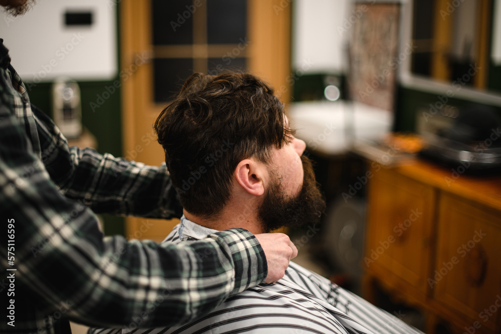 Obraz premium side view on barber fixing hairdressing collar around neck of man client.