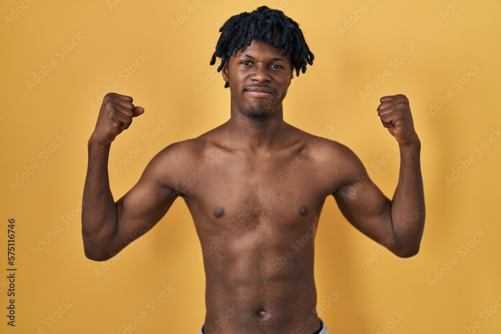 Young african man with dreadlocks standing shirtless showing arms muscles smiling proud. fitness concept.