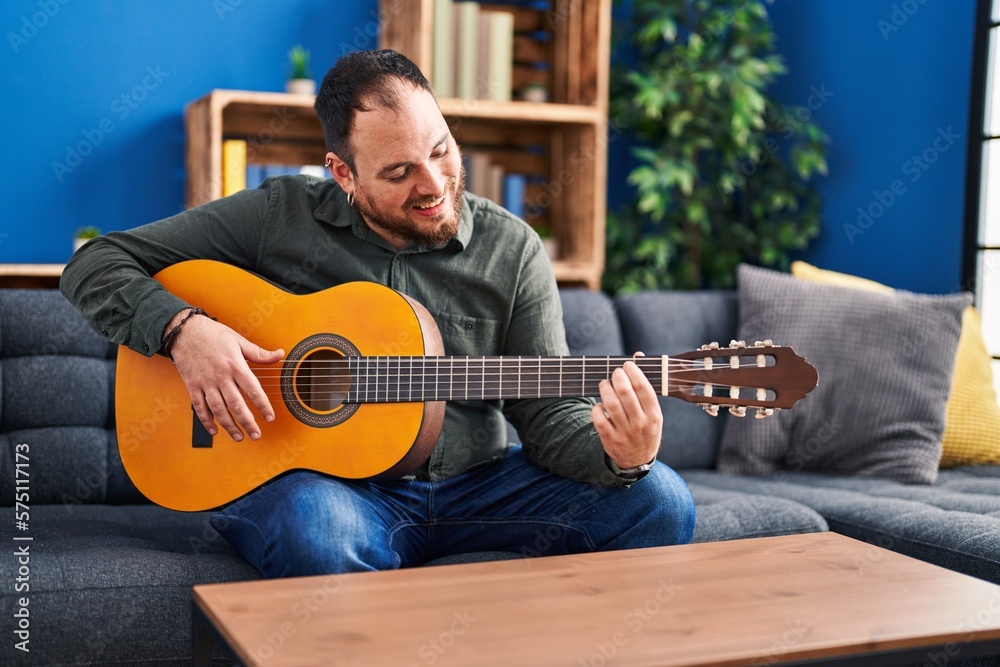 Obraz premium Young hispanic man playing classical guitar sitting on bed at home