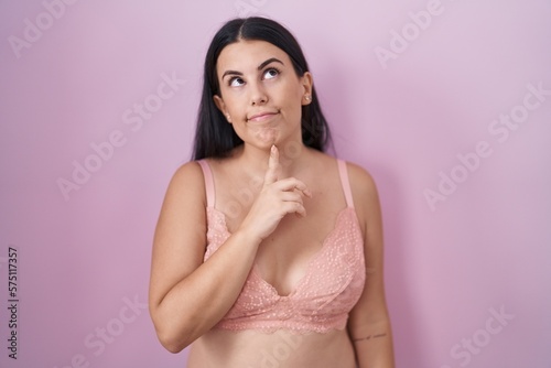 Young hispanic woman wearing pink bra thinking concentrated about doubt with finger on chin and looking up wondering