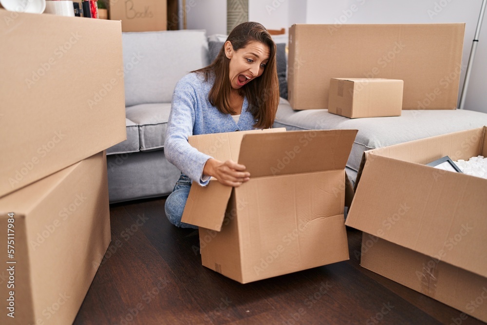 Young woman moving to a new home looking inside cardboard box celebrating crazy and amazed for success with open eyes screaming excited. Young woman moving to a new home looking inside cardboard box celebrating crazy and amazed for success with open eyes screaming excited.