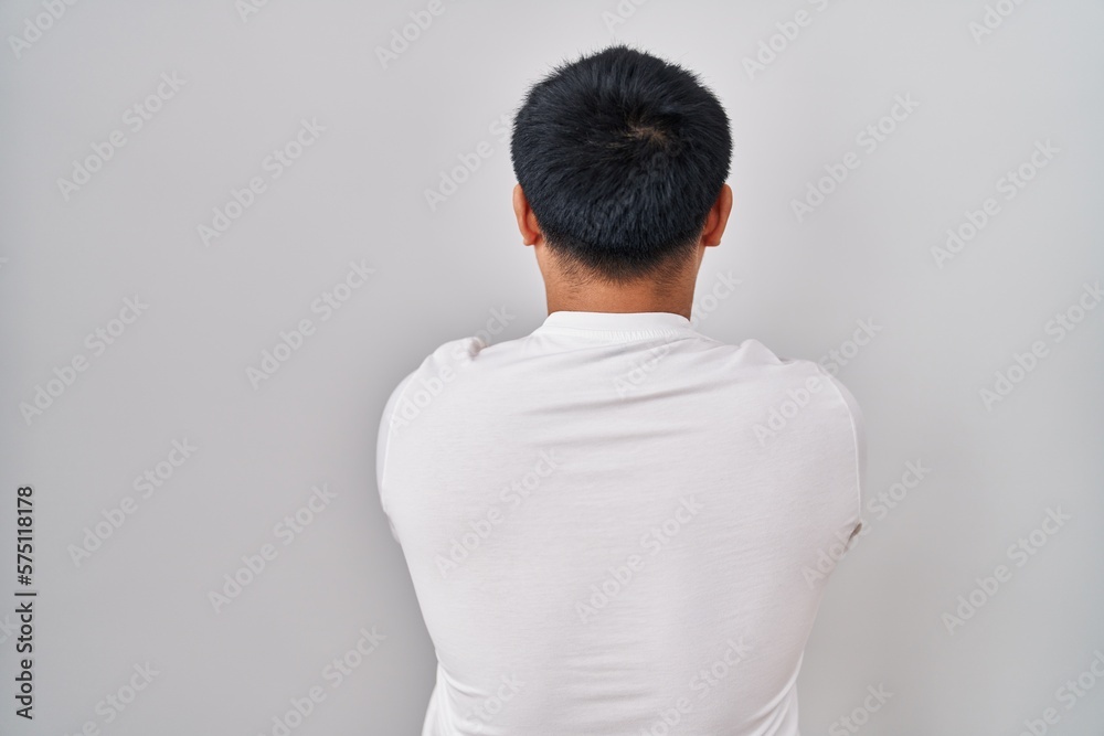 Young chinese man standing over white background standing backwards looking away with crossed arms