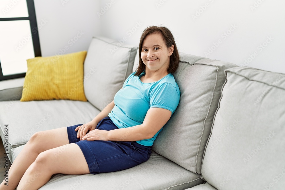 Brunette woman with down syndrome sitting on the sofa at the living room Brunette woman with down syndrome sitting on the sofa at the living room