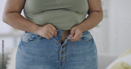 Closeup of one slightly overweight female struggling to put on her denim pants in the room at home. Womans pants not fitting due to gained weight around her waist and hip area at home in the bedroom