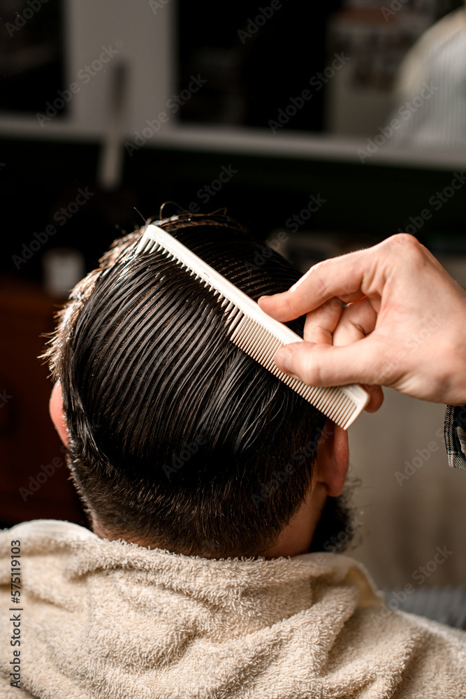Naklejka premium rear view of male head with wet hair and hand of barber gently combing hair