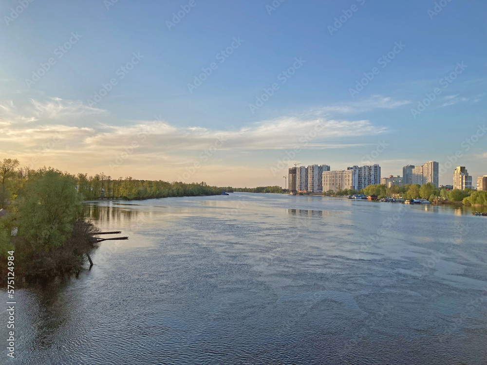 View of the deep river with the buildings in the background. Beautiful panoramic view of the city of Kyiv Dneper River at sunset on dark blue water with glowing reflected rays of the sun, copy-space