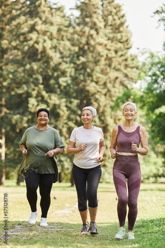 Vertical full length portrait of three senior women running towards camera in park and enjoying sports