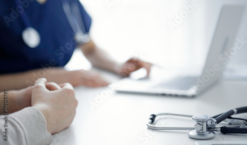 Stethoscope lying on the tablet computer in front of a doctor and patient using laptop computer at the background. Medicine  healthcare concept
