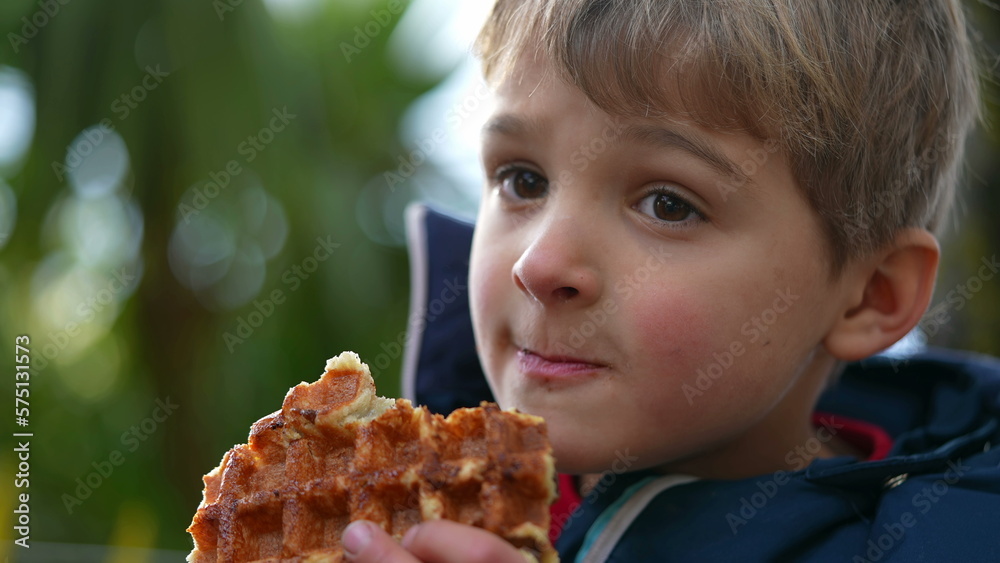 One pensive child eating waffle. Small boy eats street food outdoors during winter season