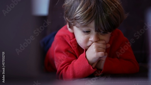 Portrait of kid lying on sofa watching cartoon. Closeup child face staring at screen with hand in chin